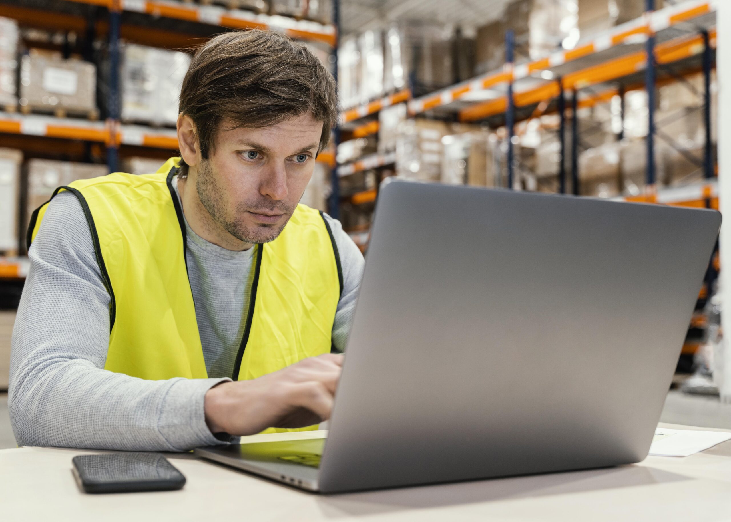 man-warehouse-working-laptop Warehouse operative researches Winfreight's inventory management software FAQs on a laptop in a warehouse environment.